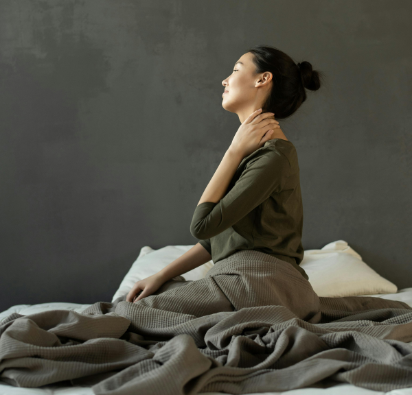 Women sitting on her bed holding her neck in pain