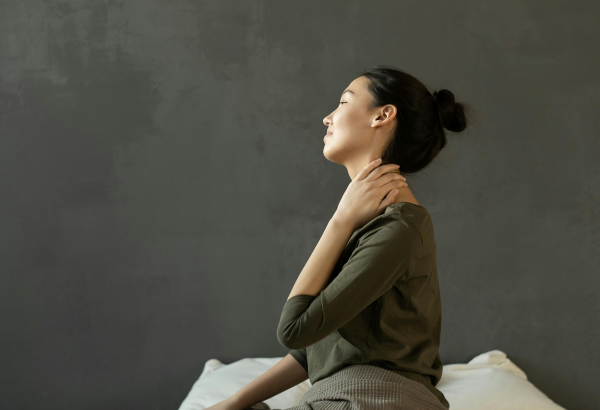 Women sitting on her bed holding her neck in pain
